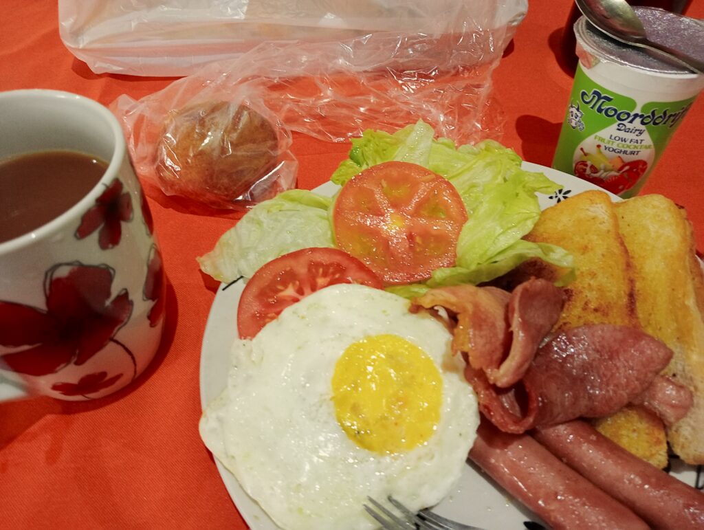 スーパーマーケットで購入した朝食セット（目玉焼き、サラダ、ベーコン、ソーセージ、ハッシュドポテト）とヨーグルト、ドーナツ